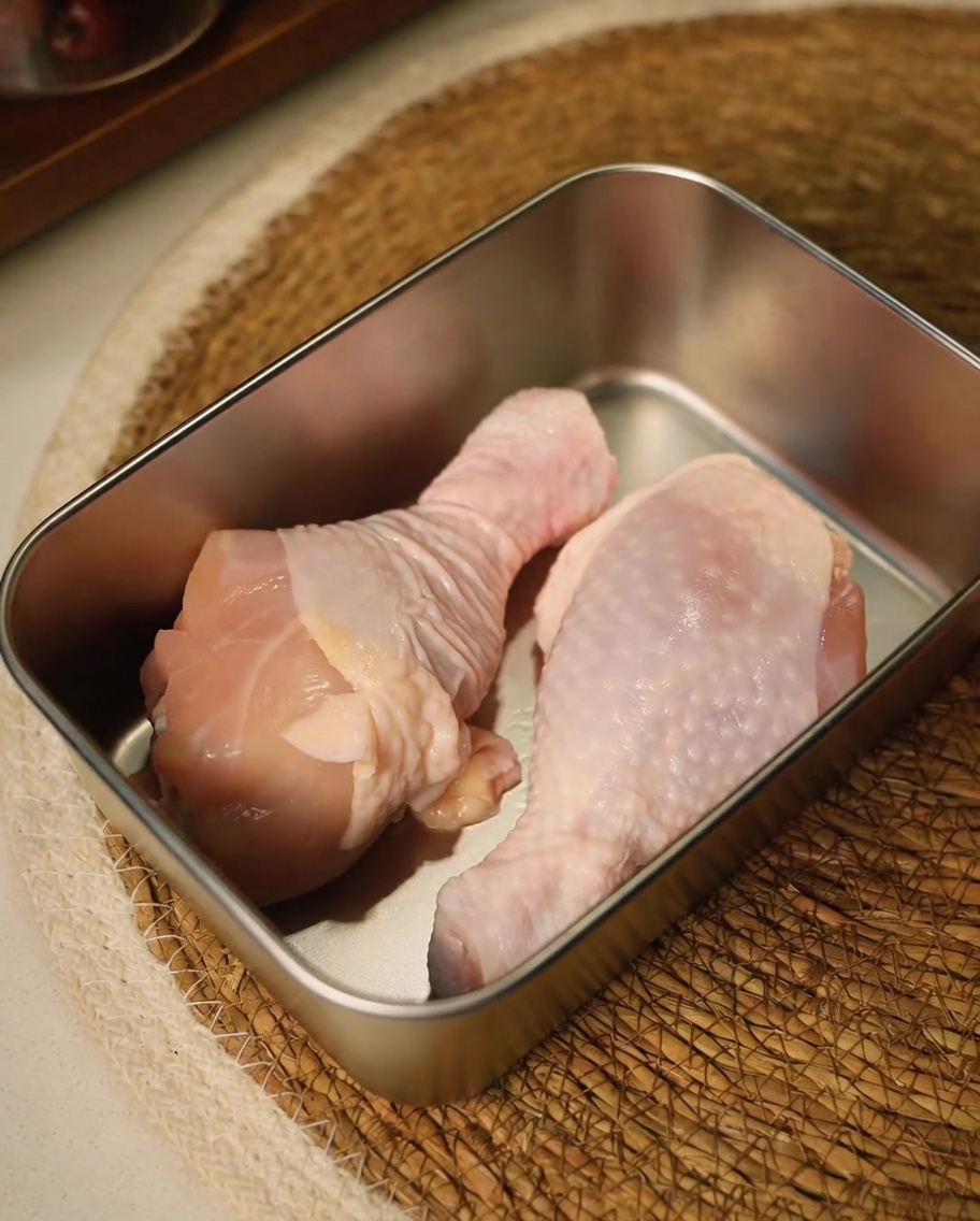 Raw chicken thighs being trimmed with kitchen scissors in a metal container.