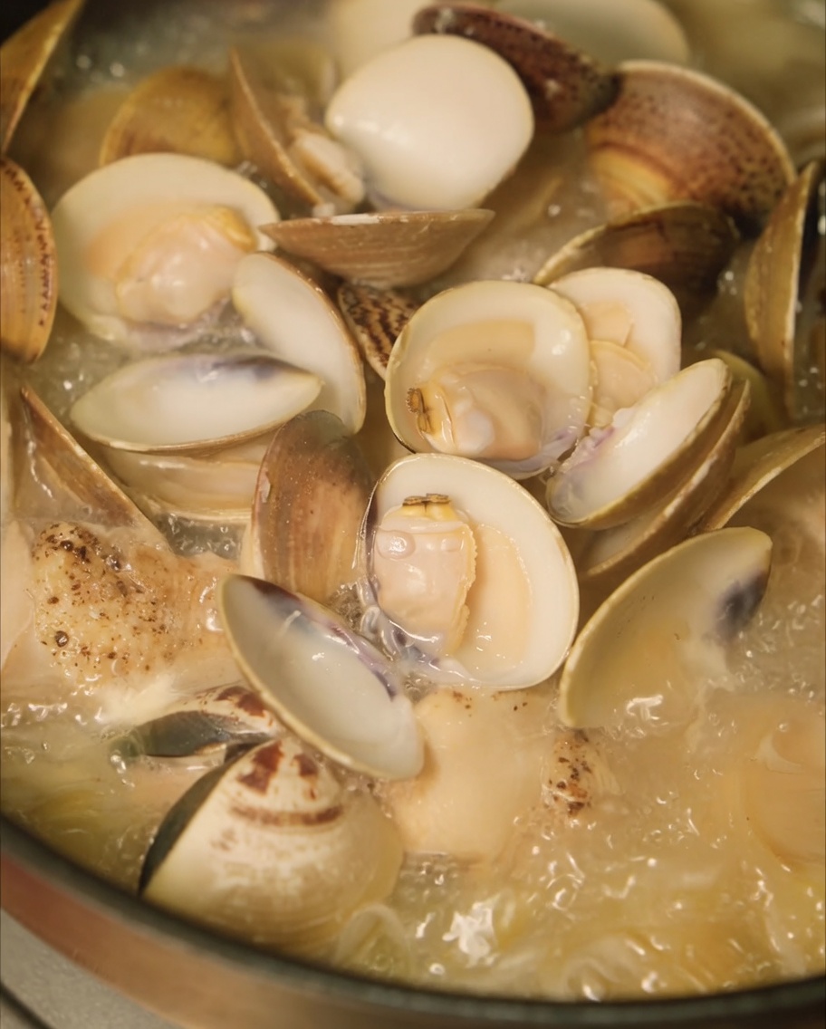 Fresh clams being added to the pot of chicken and onion soup to steam.