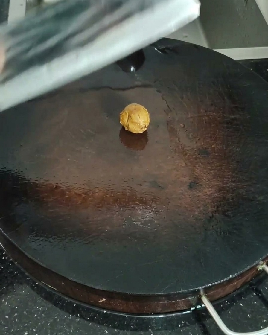 A close-up of sand ginger being smashed with a meat cleaver on a wooden board.