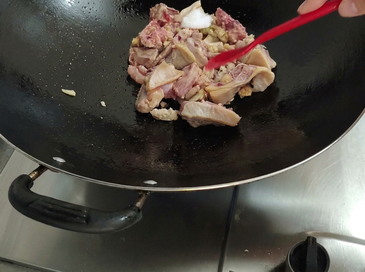 Adding salt to the chicken in the wok using a red spatula.