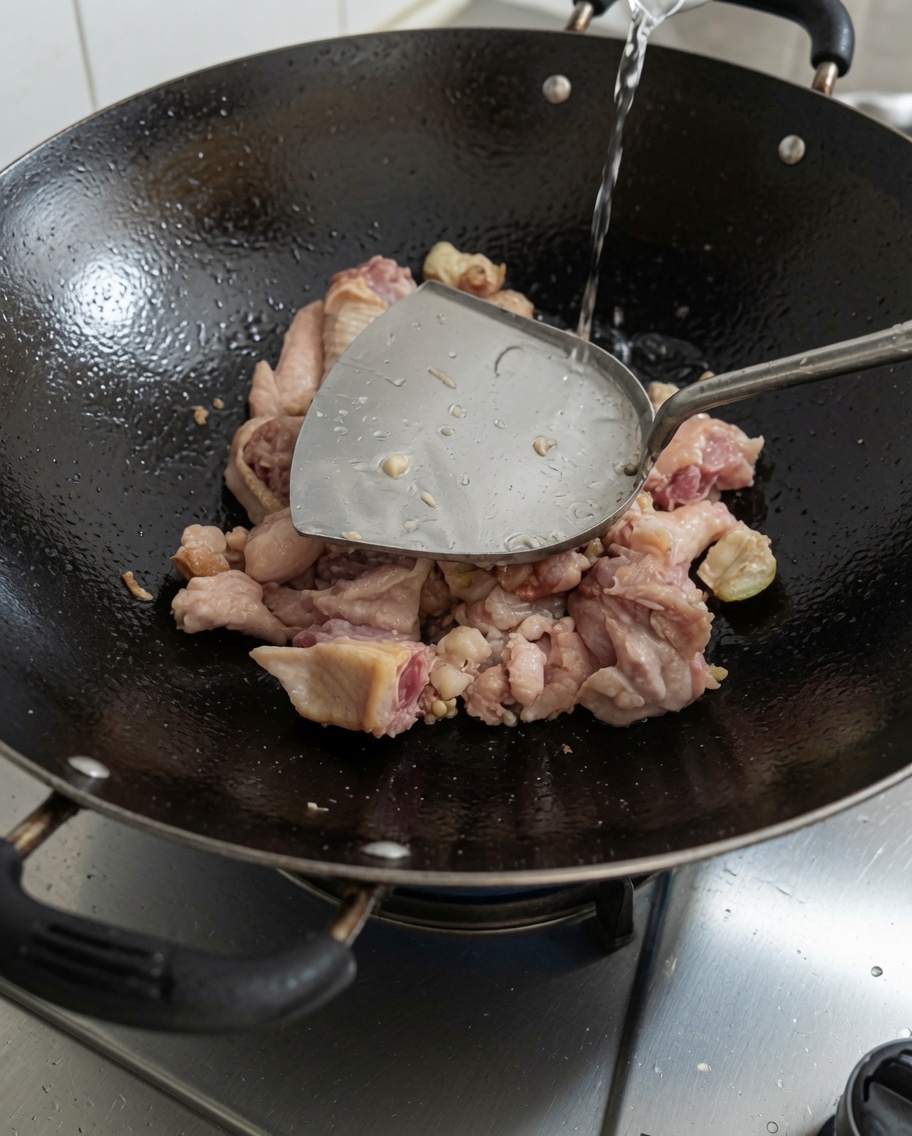 Pouring fresh water into the wok containing seared chicken.