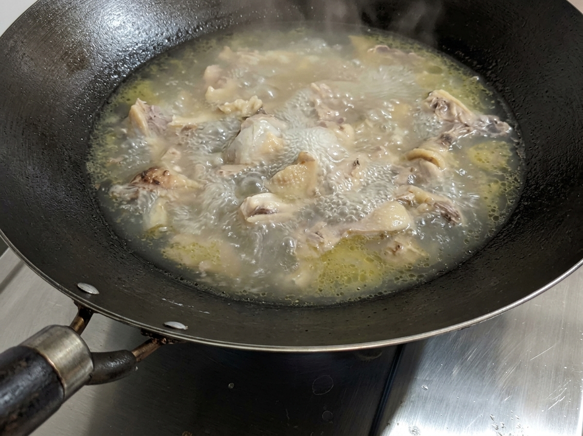 A simmering chicken soup with salt being added.