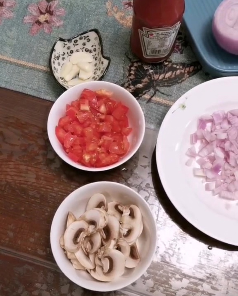 A bowl of freshly chopped tomatoes, sliced mushrooms, and minced garlic on a table.