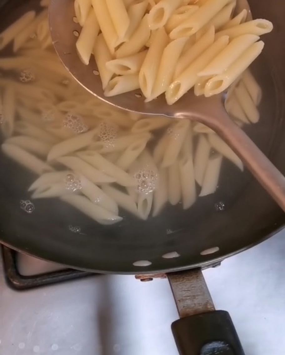 Penne pasta being lifted from boiling water with a large slotted spoon.