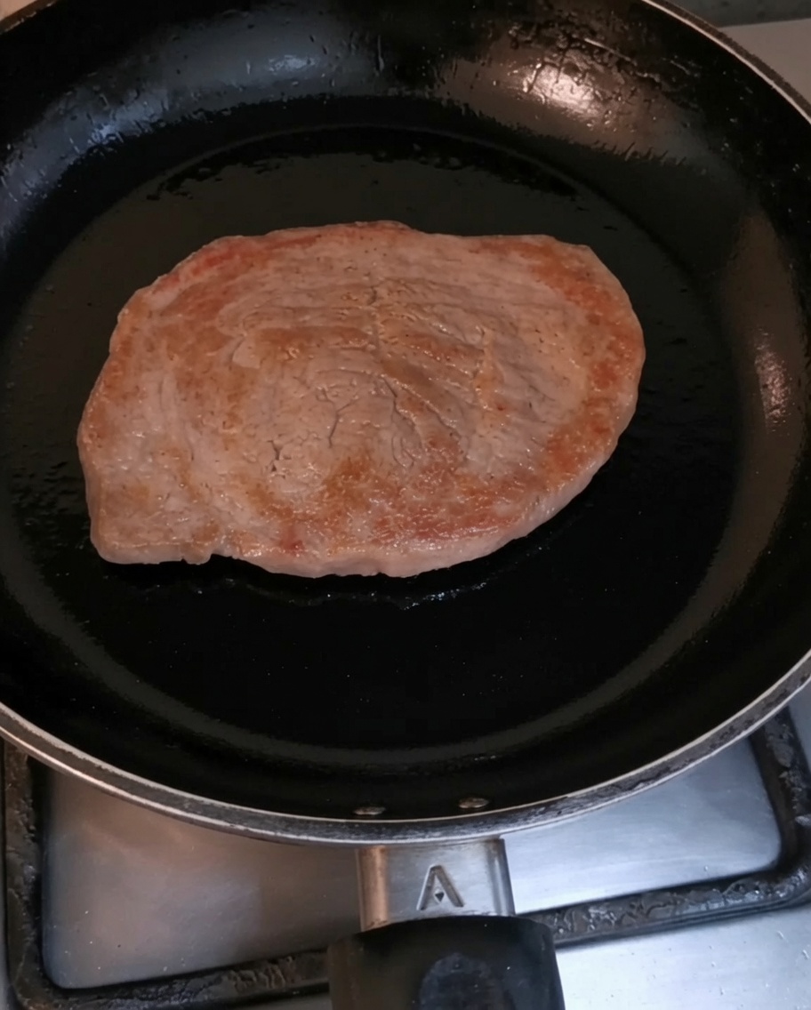 A fillet steak browning in a hot black skillet.