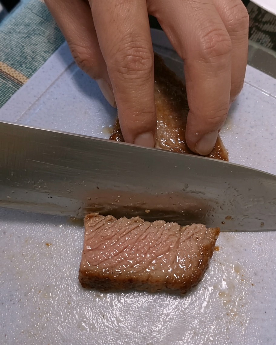 Hands slicing a seared steak on a plastic cutting board.