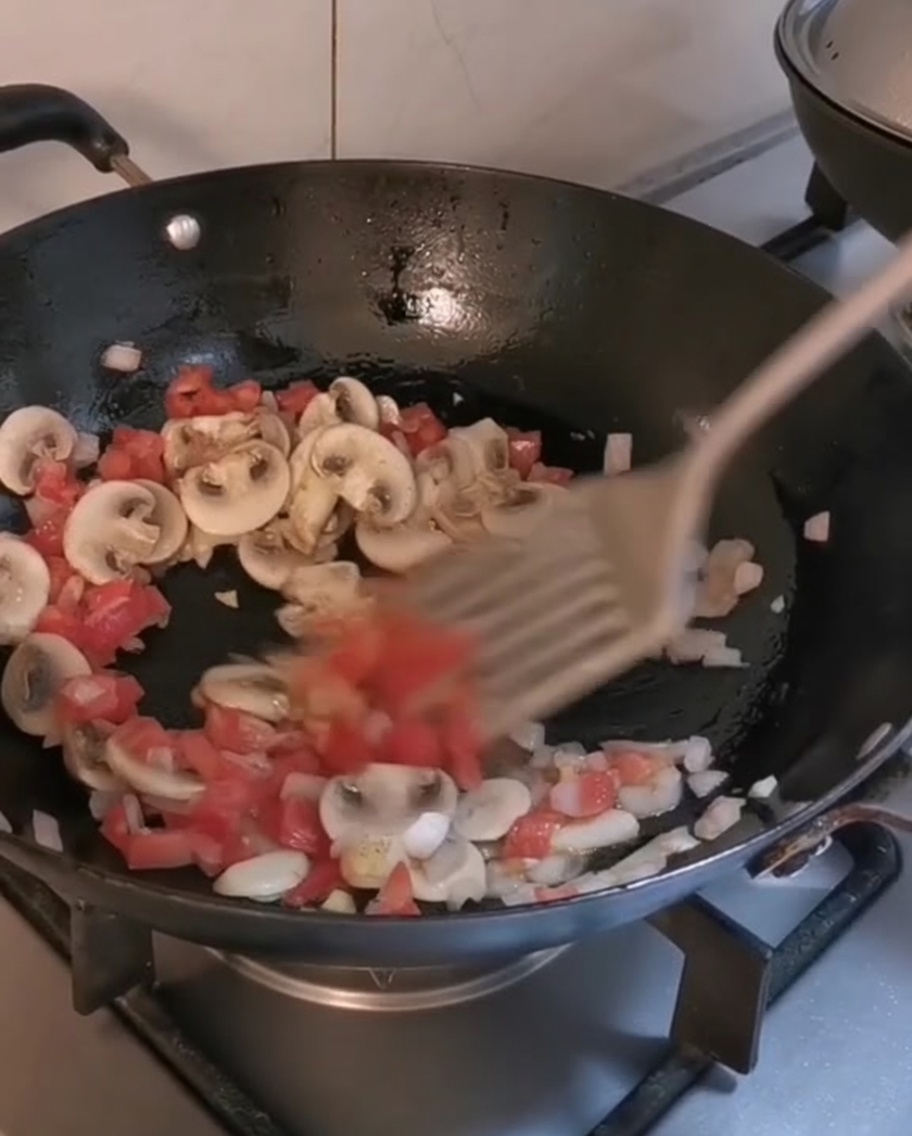 Mixing cooked penne and steak strips into a wok with sautéed vegetables.