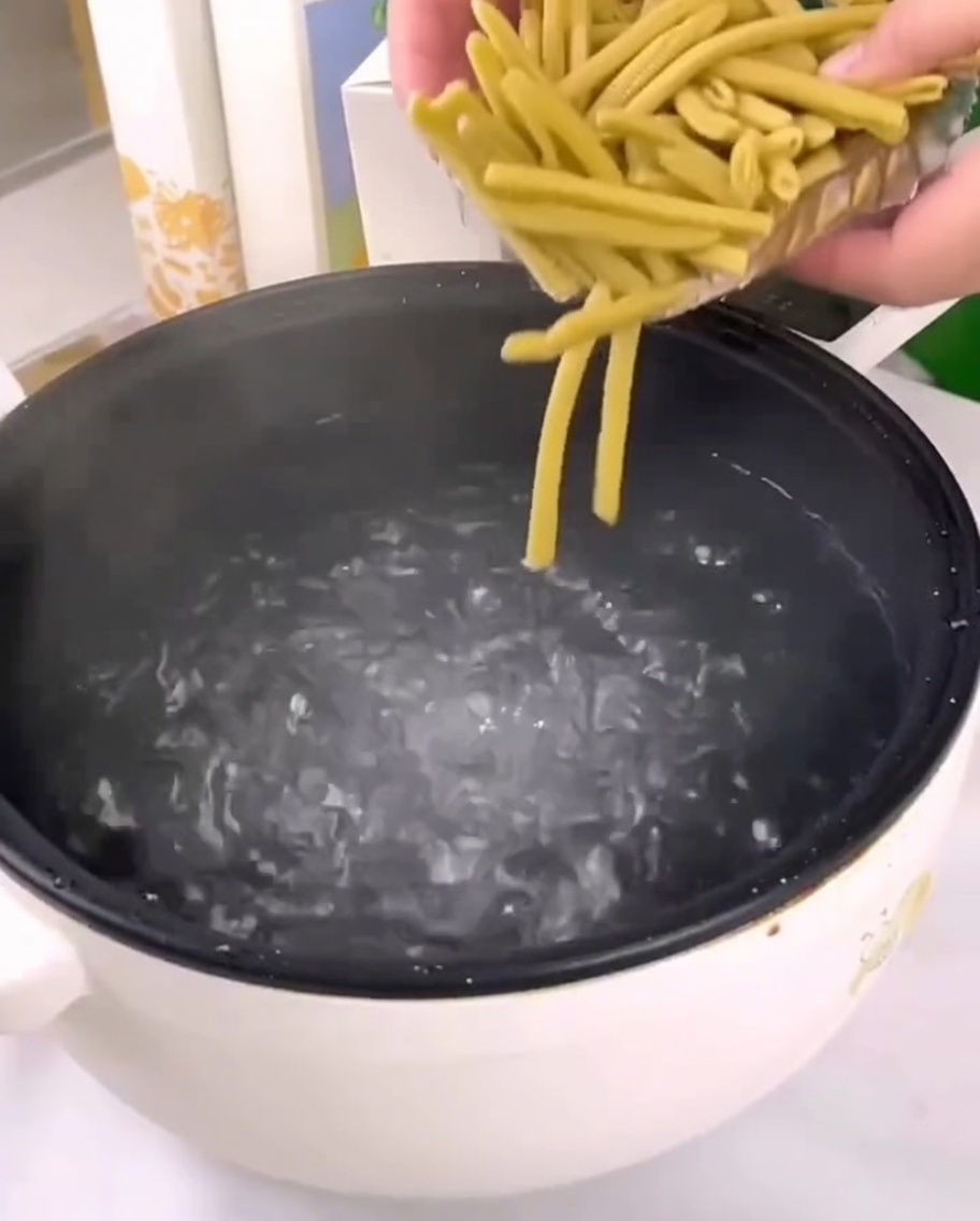 Dried millet penne pasta being poured into a pot of boiling water.