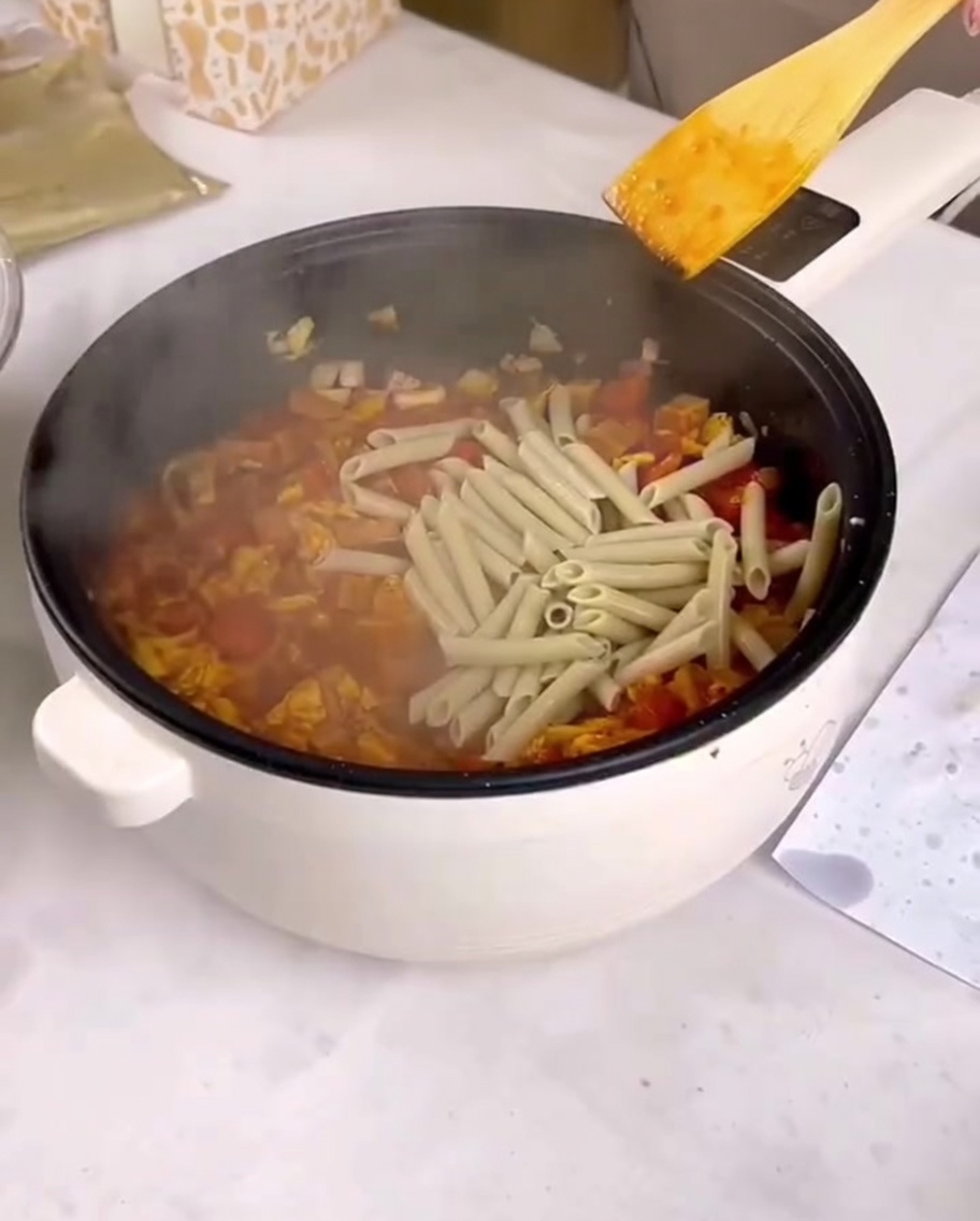 Cooked penne pasta being added to a pan with sauce and stir-fried ingredients.
