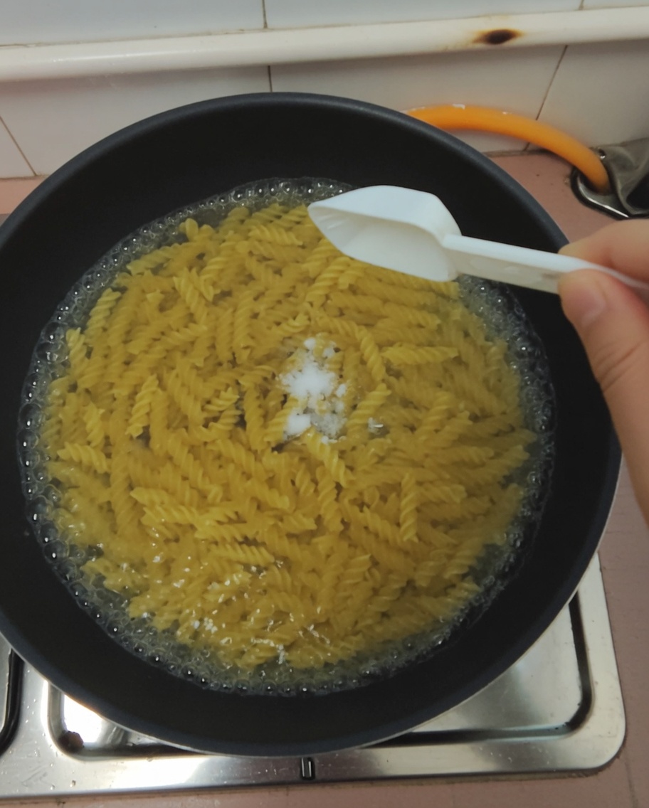 A spoonful of salt being added to a pot of boiling pasta.