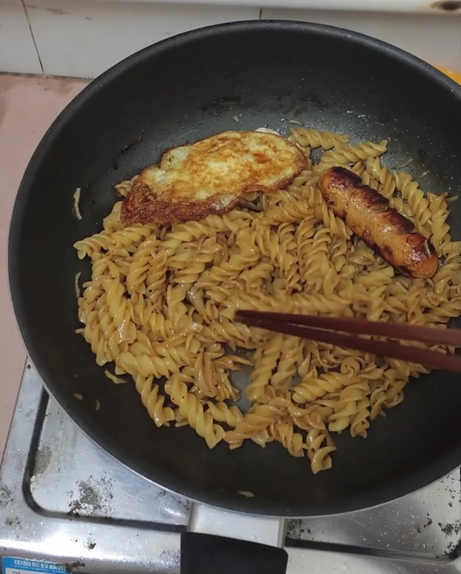 Fried egg and sausage served atop a pan of seasoned black pepper fusilli.