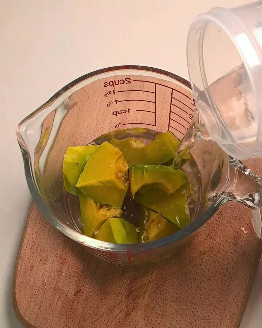 Water being poured over kabocha squash pieces in a glass measuring cup.
