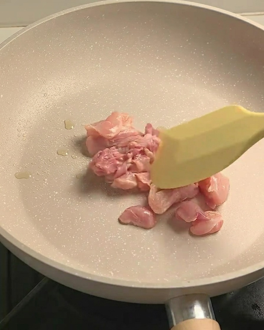 Seasoned chicken leg meat pieces stir-frying in a non-stick pan, showing light browning.