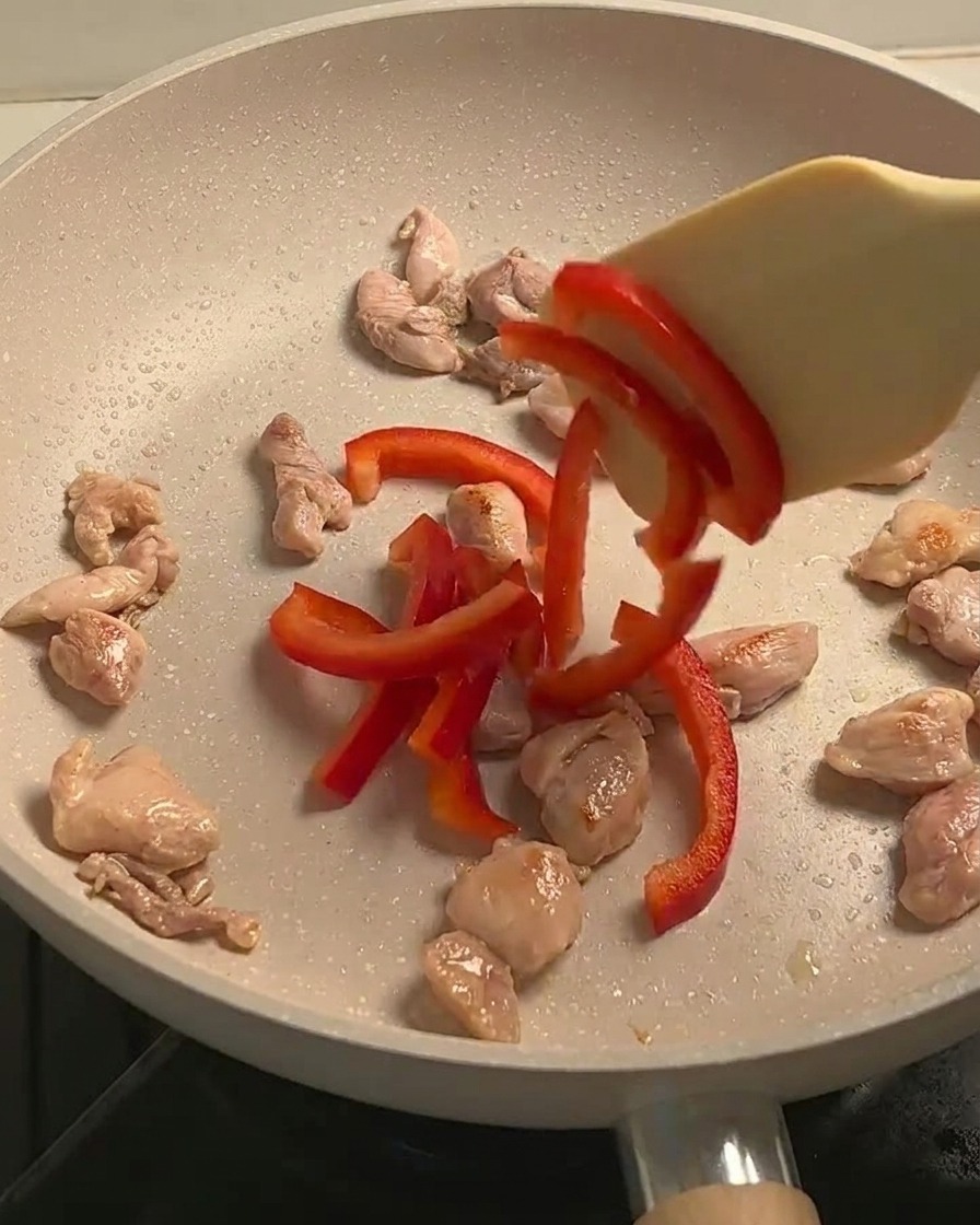 Sautéed chicken, sliced red bell peppers, and mushrooms cooking together in a pan.
