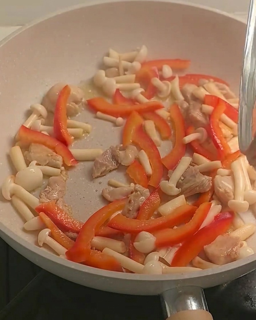 Cooked fusilli pasta being added to the pan containing stir-fried chicken and colorful vegetables.