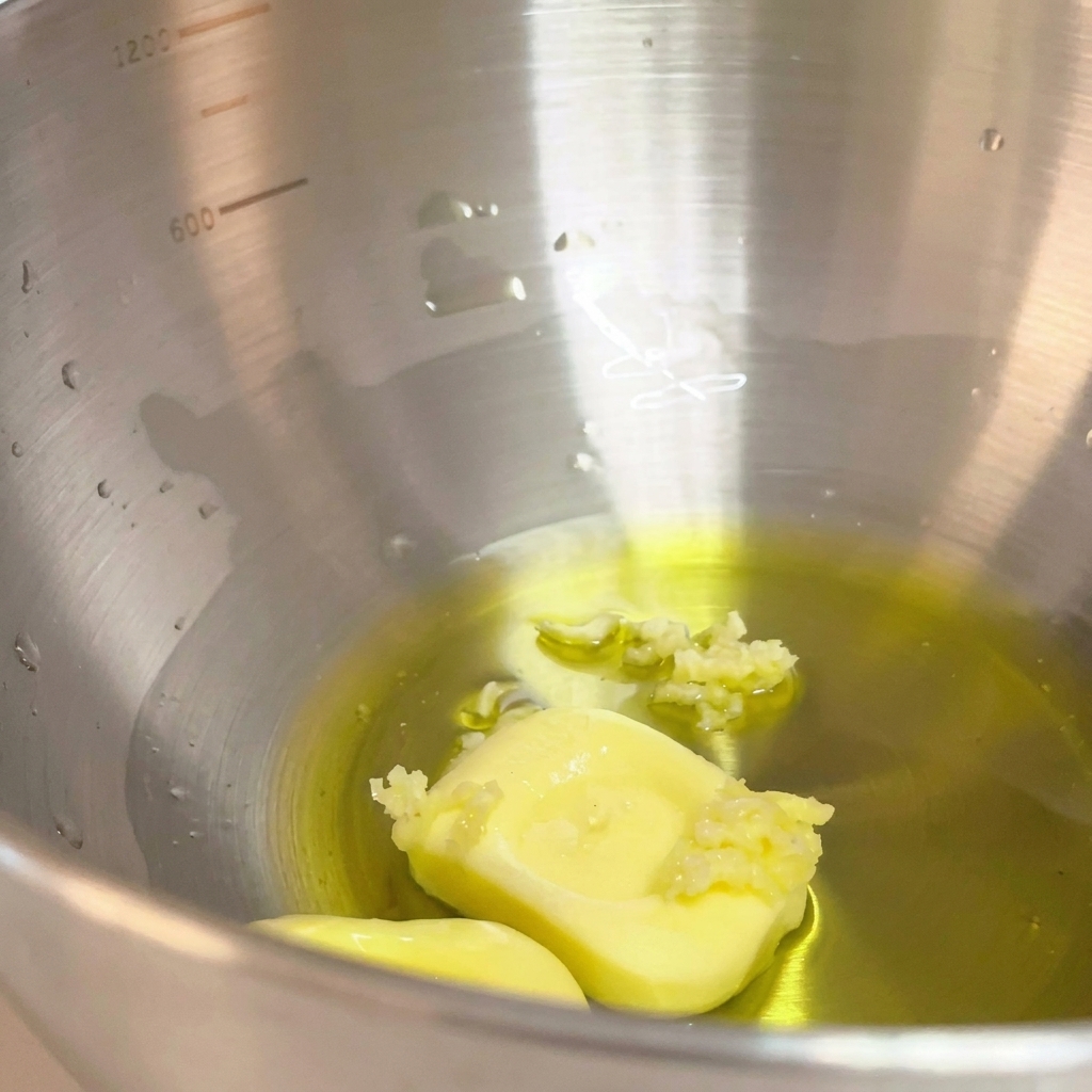 Crushed garlic added to the mixture of olive oil and butter in the metal bowl.