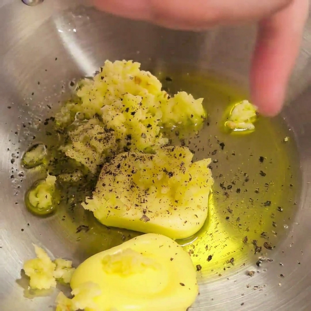 Freshly ground black pepper seasoning the mixture of butter, garlic, and olive oil in the bowl.