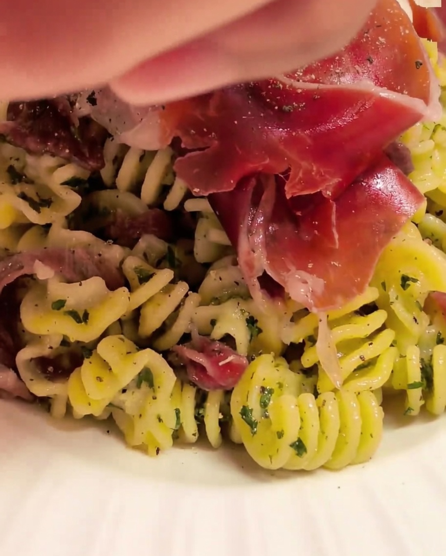 Spiral pasta being tossed in a bowl with sauce using kitchen tongs.