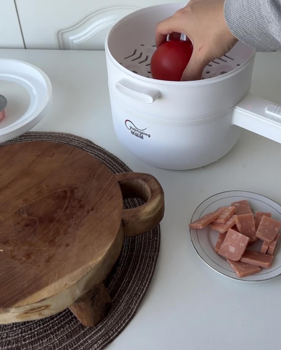 A whole fresh tomato sitting in the steamer basket atop the electric pot.
