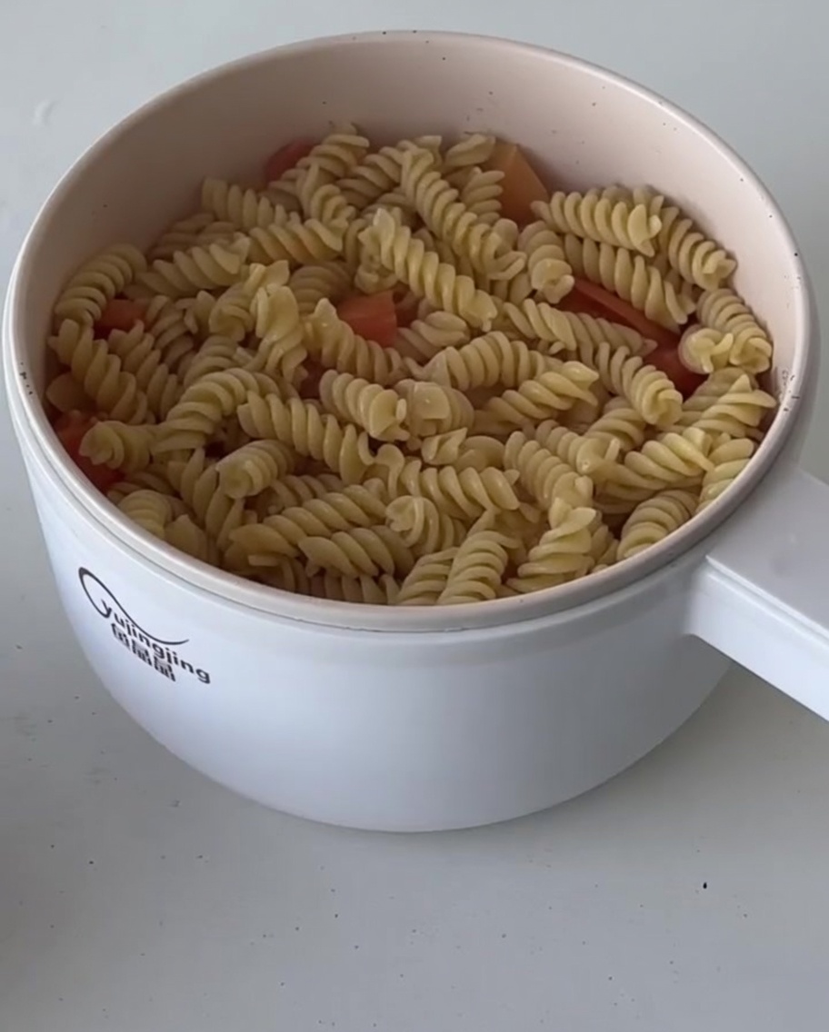 Cooked fusilli pasta being added into the pan with the tomato and bacon sauce mixture.