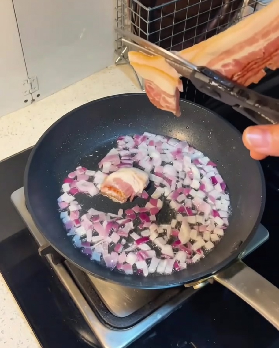 Bacon and onions stir-frying together in a pan.