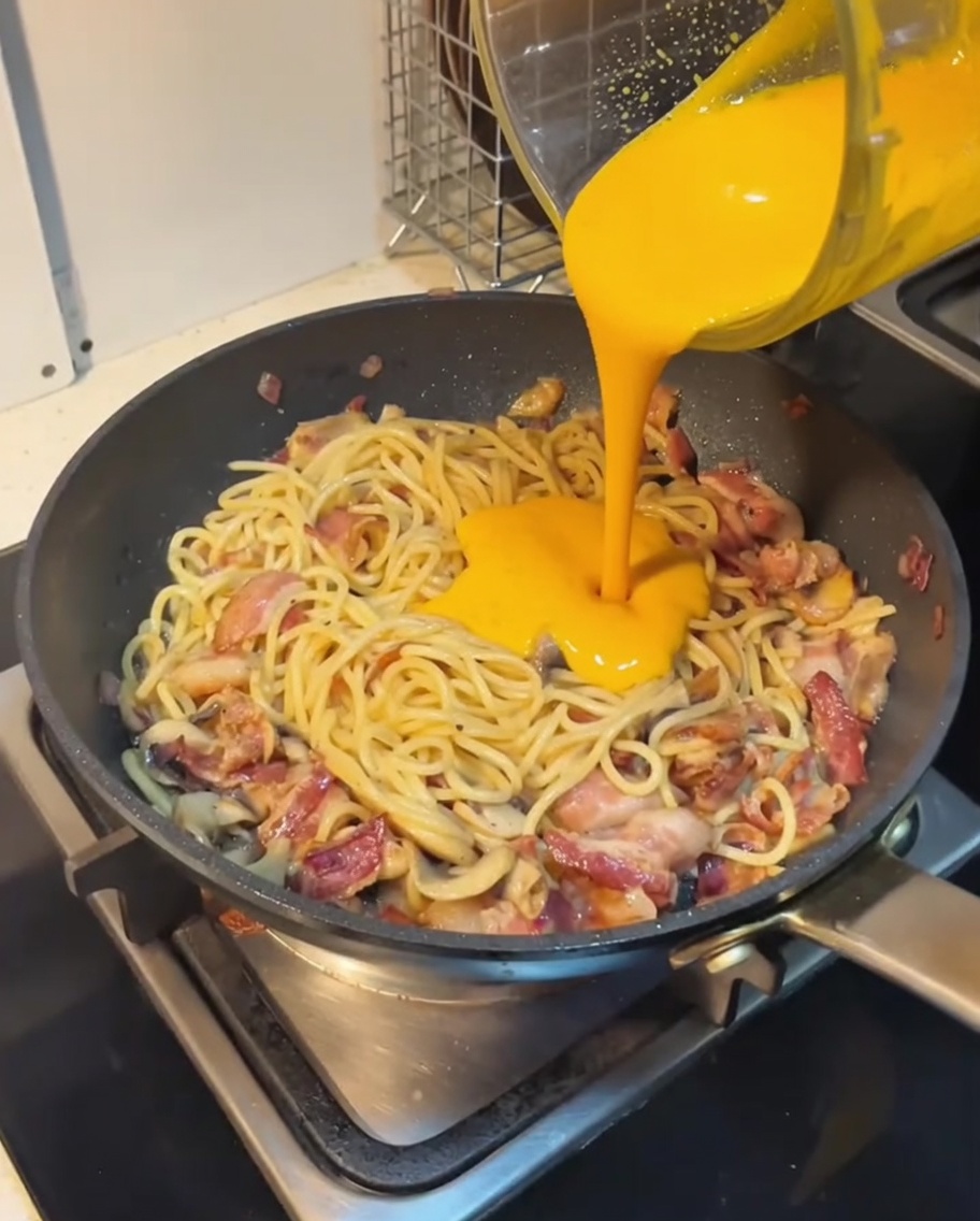 Rich, creamy orange pumpkin sauce being poured over pasta in a pan, creating a smooth, even coating.