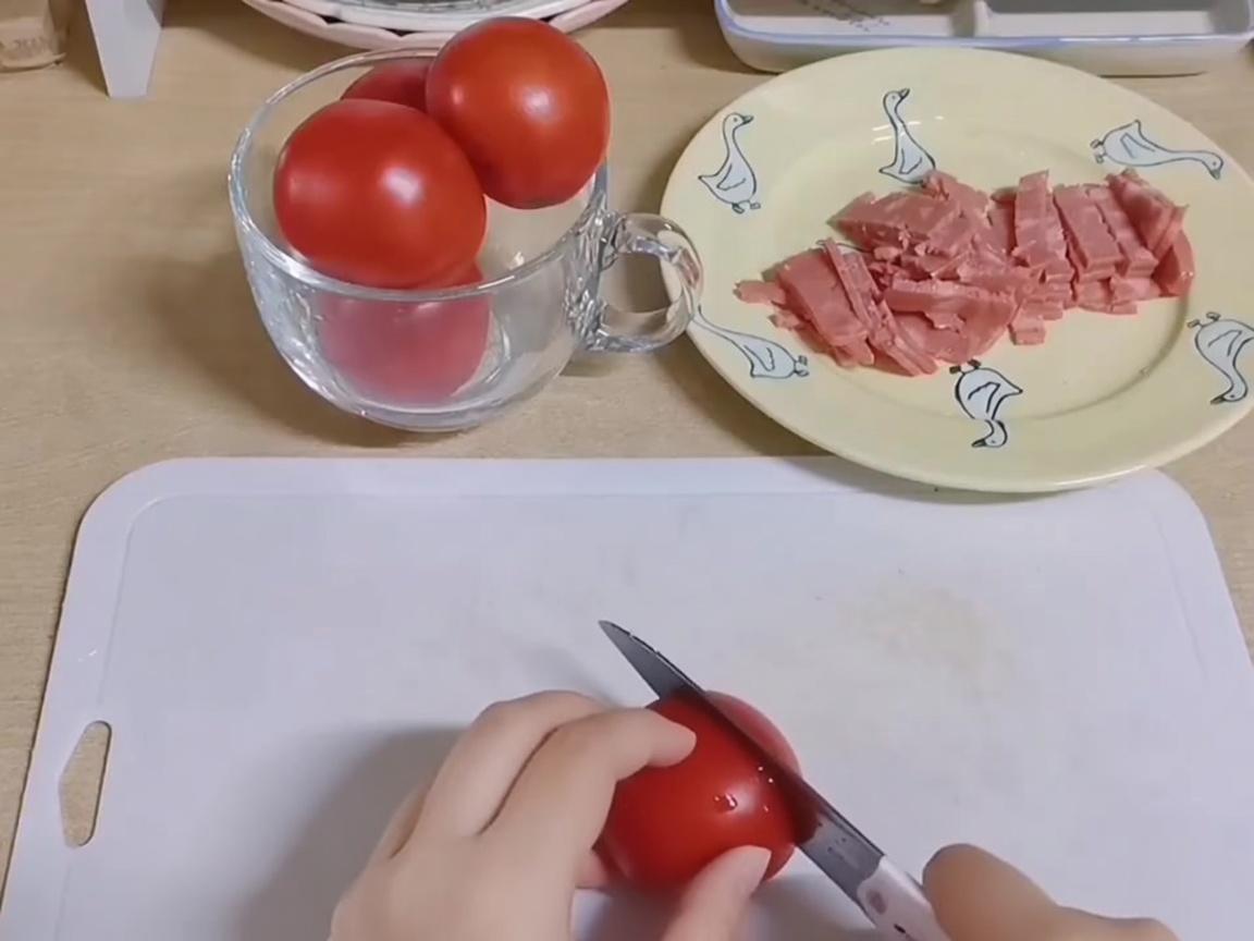 Hands using a knife to chop fresh red tomatoes into small pieces on a white cutting board.