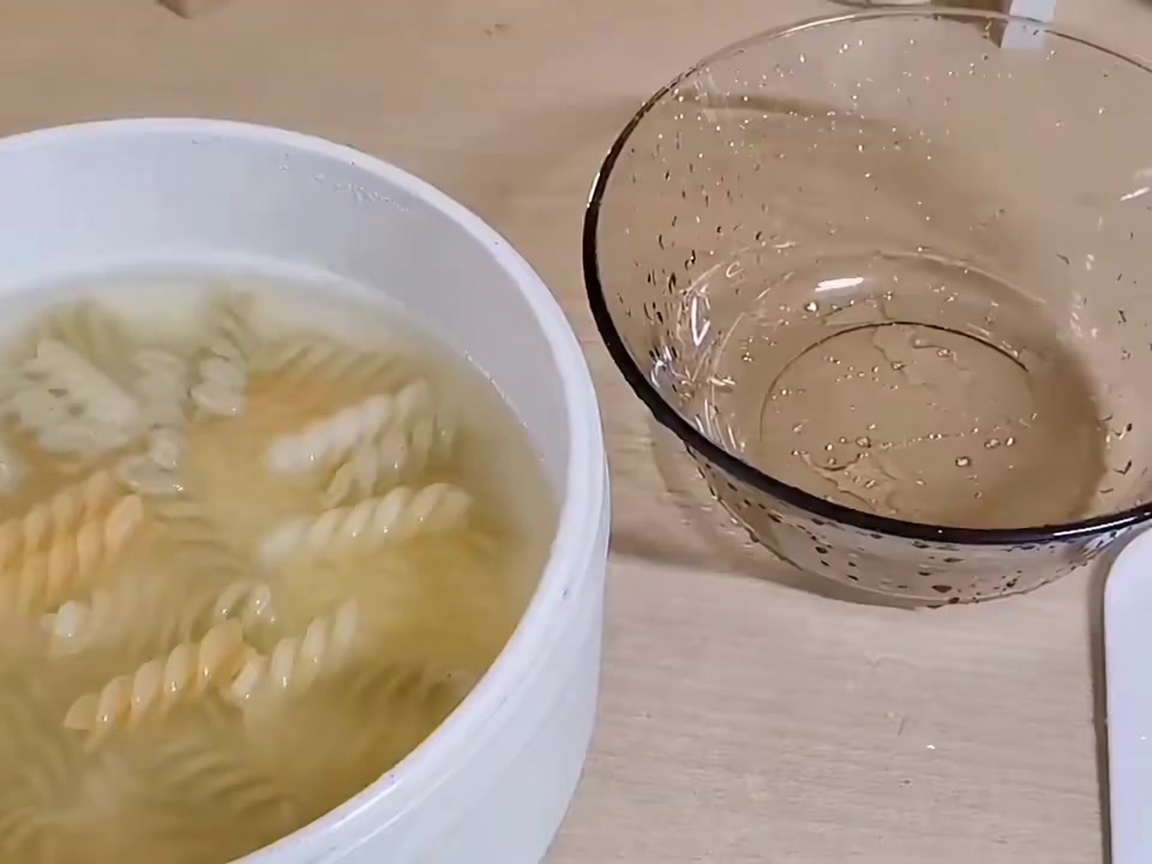Cooked spiral pasta being ladled out of a pot into a separate bowl.