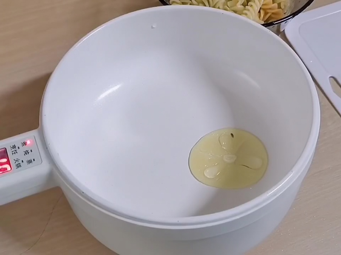 Thin slices of garlic sizzling in a pool of hot oil inside a white cooking pan.