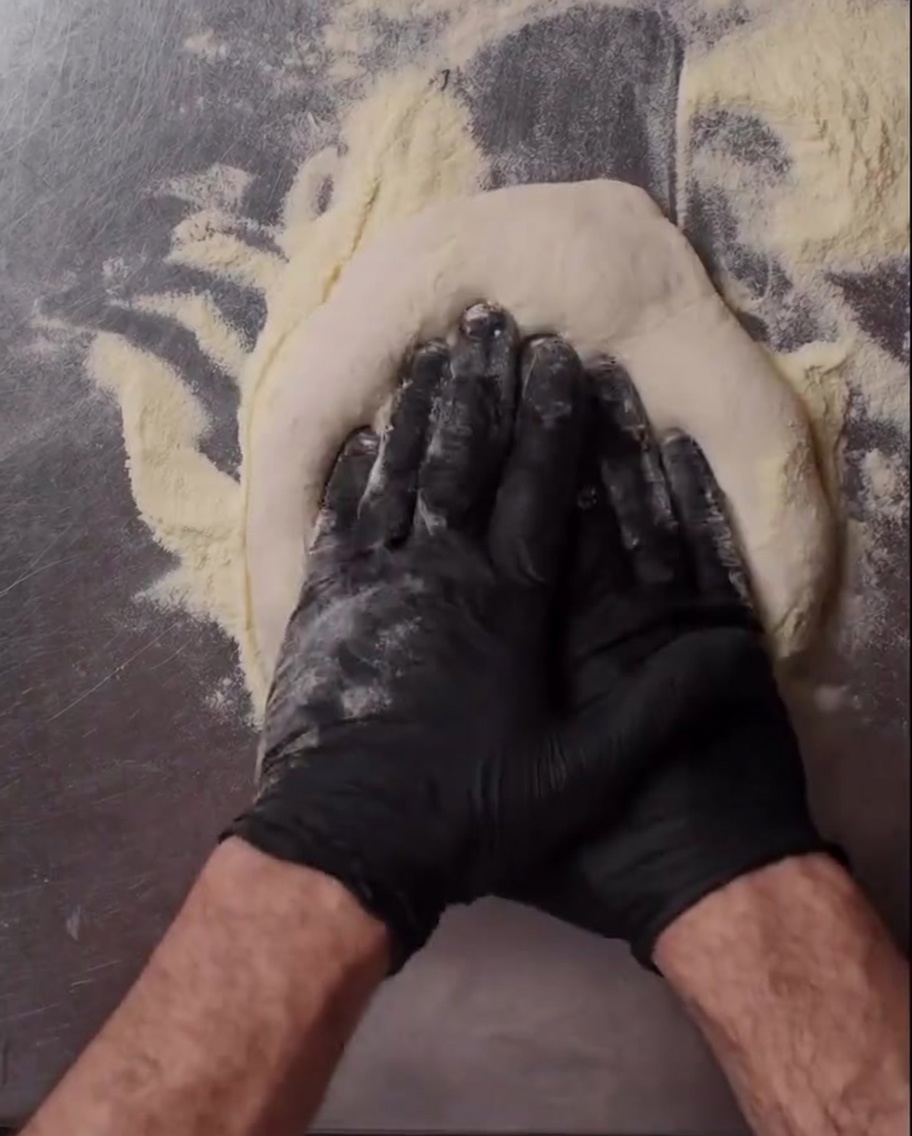 A close-up view of hands stretching pizza dough on a floured surface.