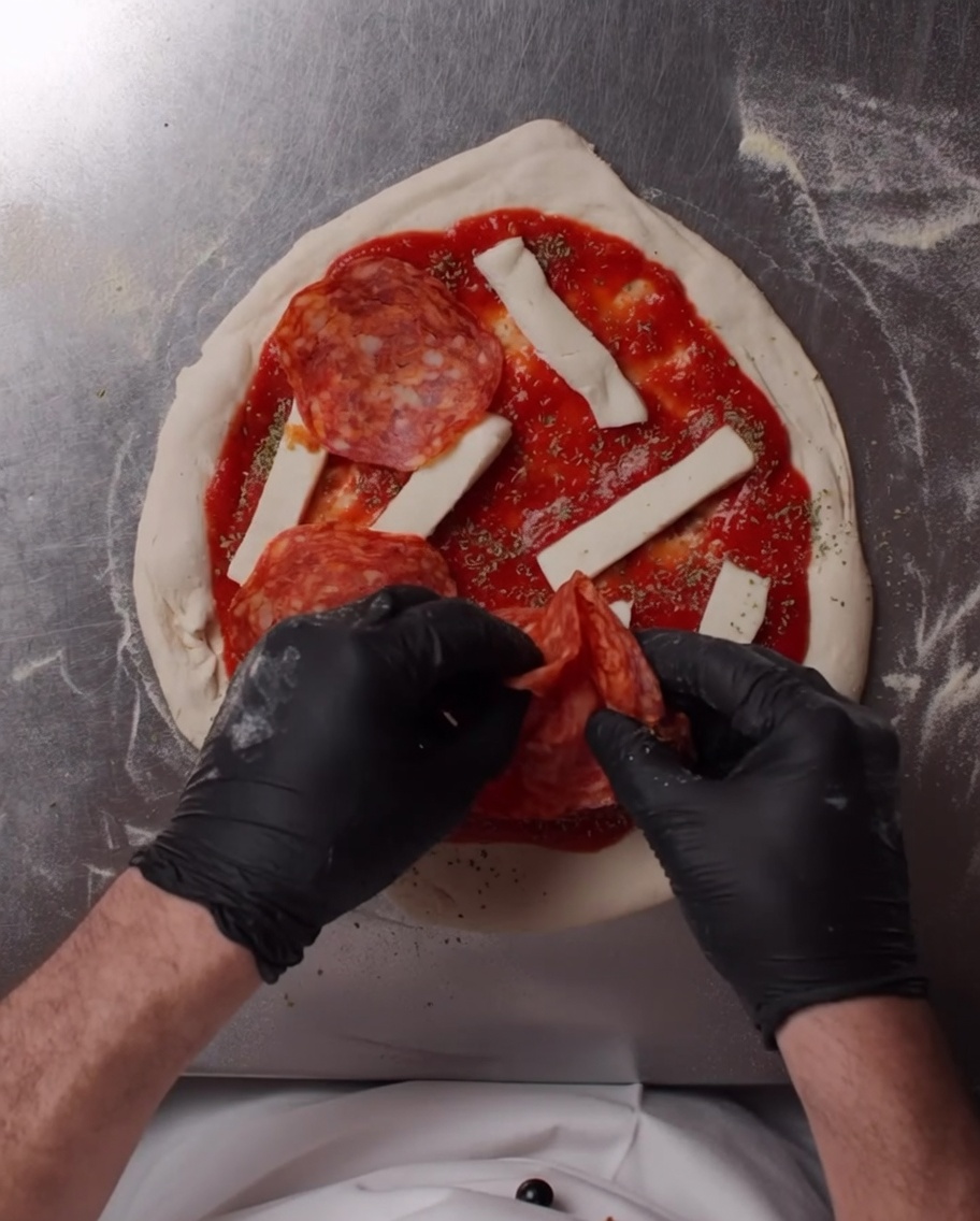 Spicy salami slices being arranged on top of the mozzarella cheese.