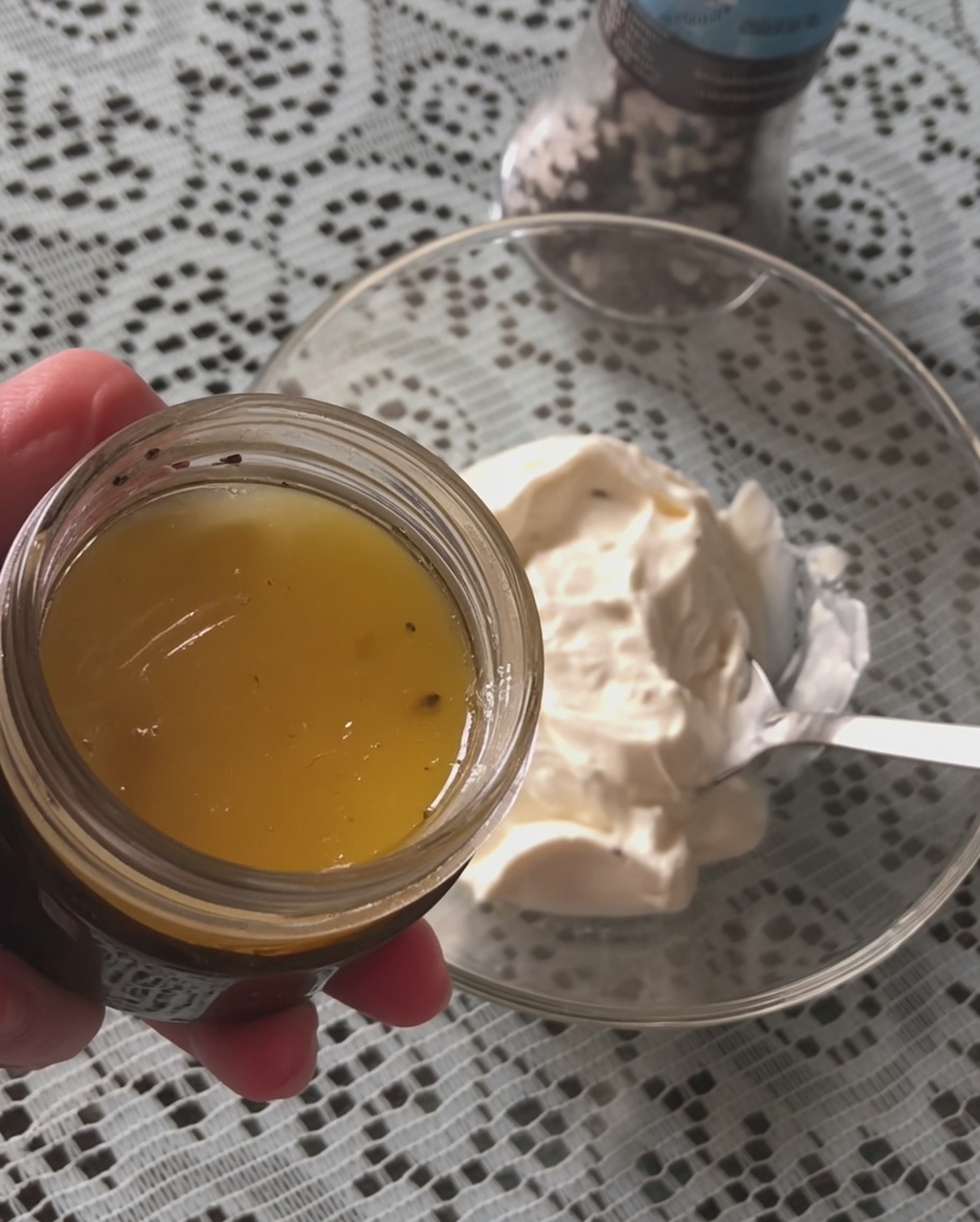 A spoonful of black truffle sauce being added to a bowl of white sour cream.