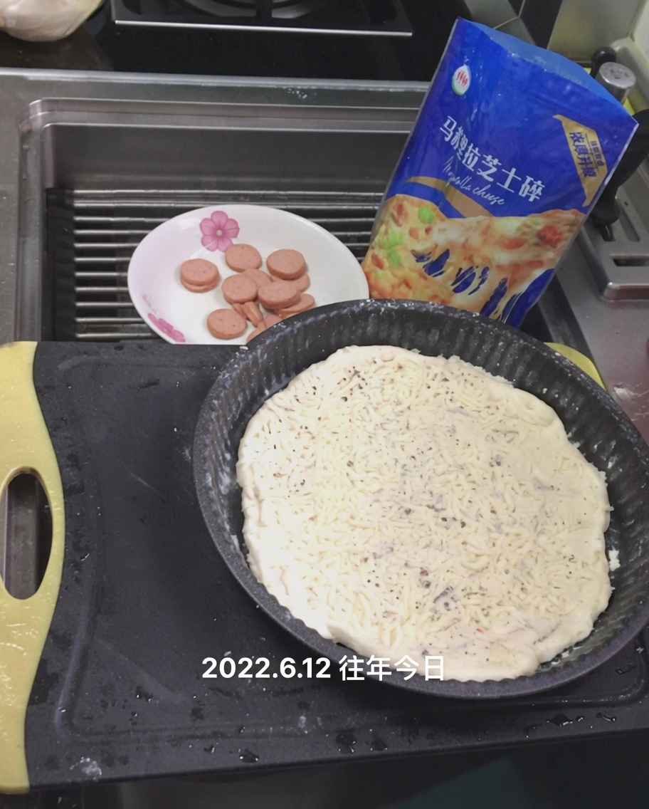 Shredded mozzarella cheese being sprinkled over the white sauce on the pizza dough.