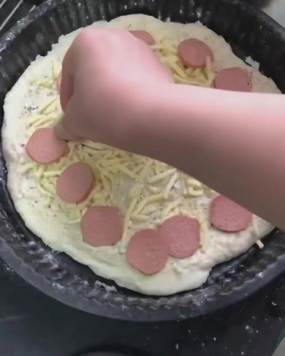 Sausage slices being placed onto the bed of shredded mozzarella cheese on the pizza.