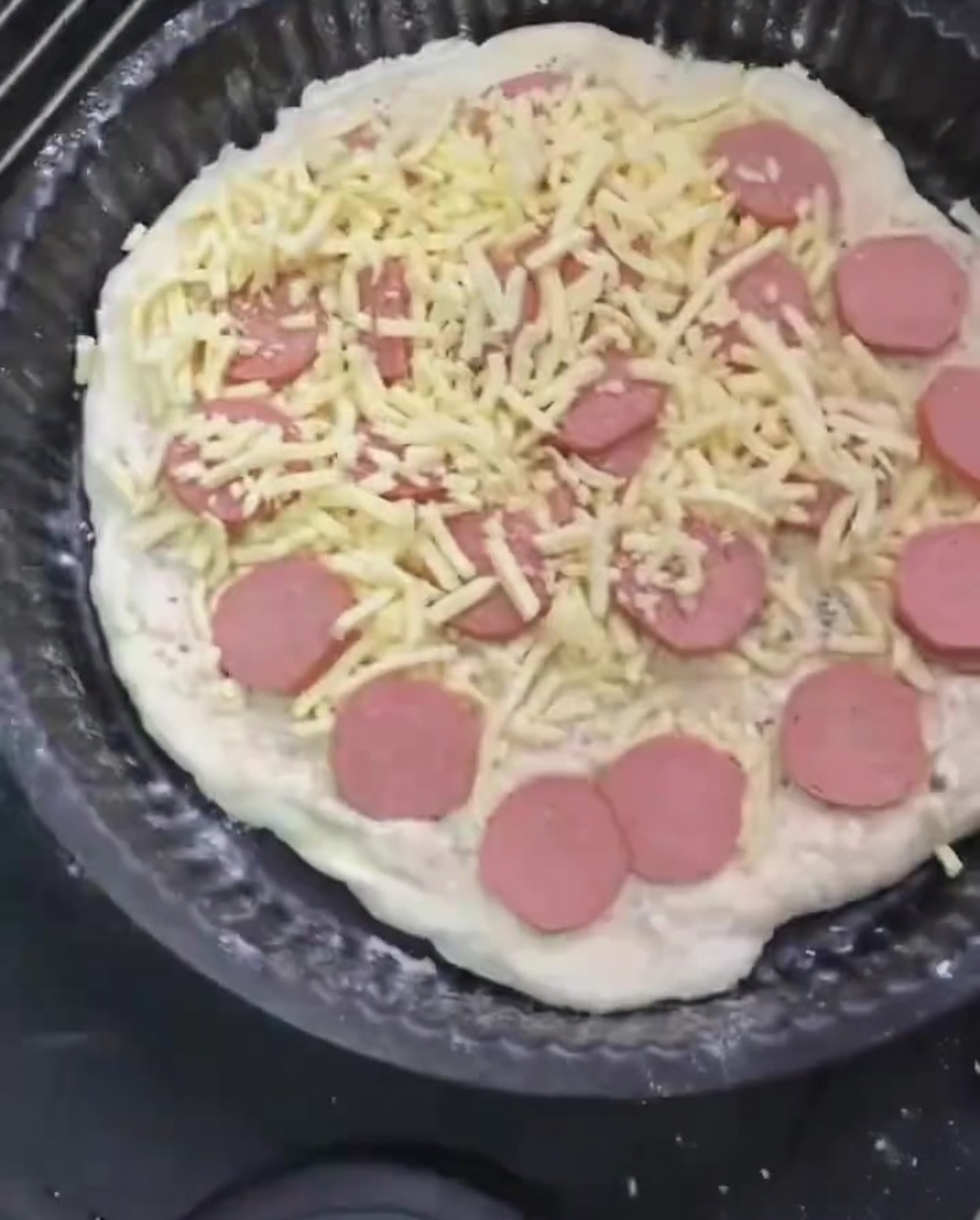 A final generous layer of shredded mozzarella cheese being spread over the sausage-topped pizza.