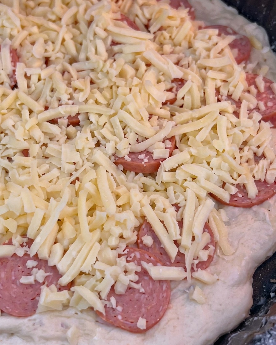 The pizza being slid into the hot oven to begin the 10-minute baking process.