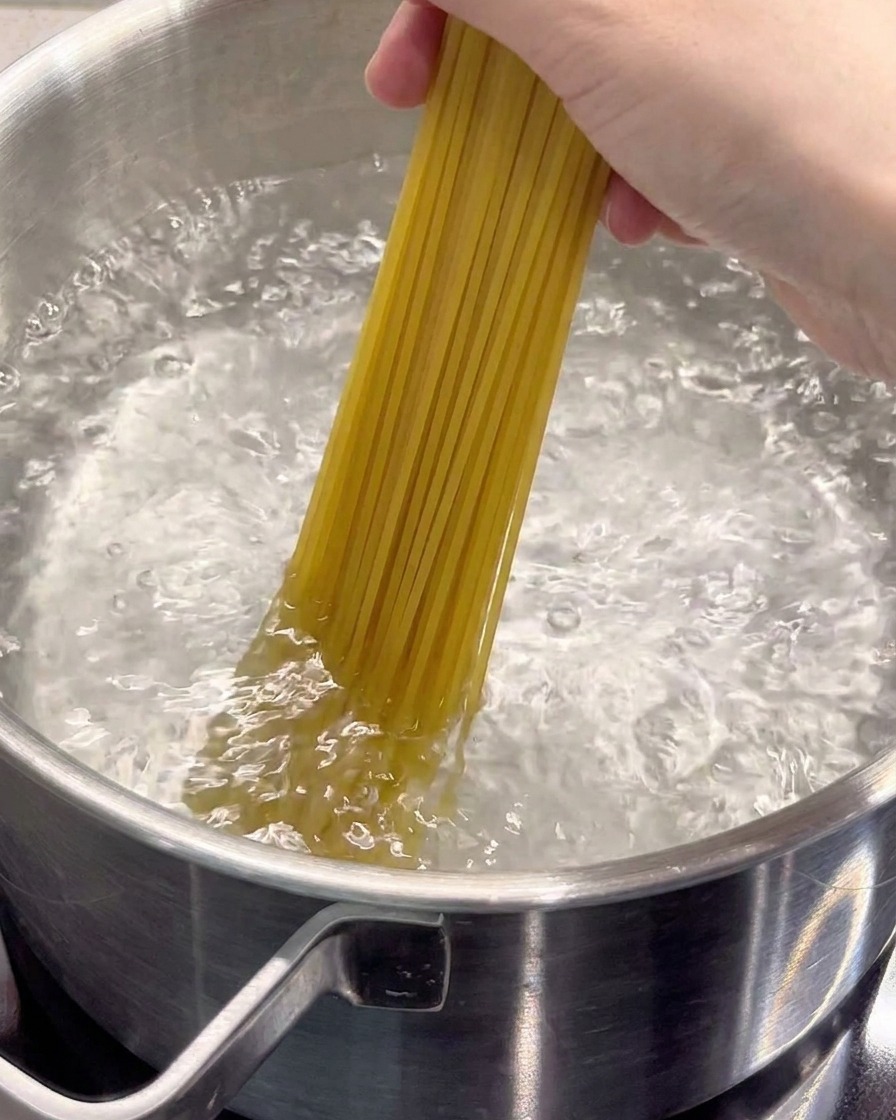 Dry spaghetti being lowered into a pot of rolling boiling water.