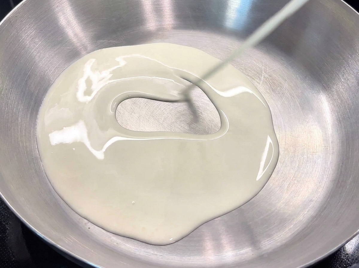 Pouring thick heavy cream into a stainless steel pan to form the base of the pasta sauce.