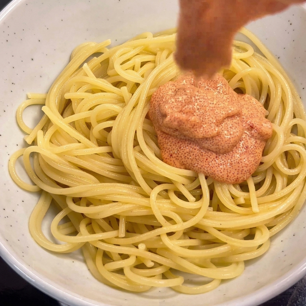 Adding Mentaiko sauce onto spaghetti in a bowl and mixing with chopsticks.