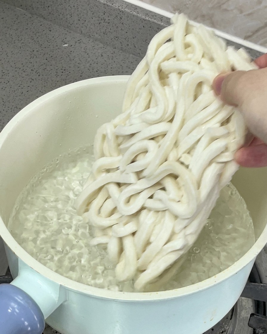 Udon noodles being submerged into a pot of boiling water for cooking.