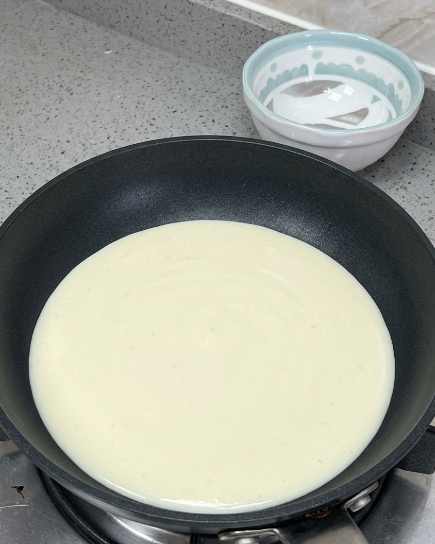 Cream, milk, butter, and mentaiko sauce being heated together in a pan to form a creamy base.