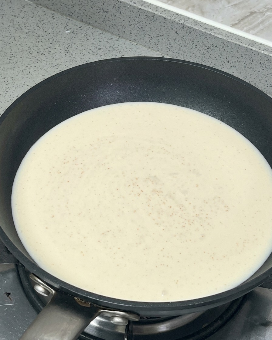 Adding salt and sugar to the simmering cream sauce in the frying pan.