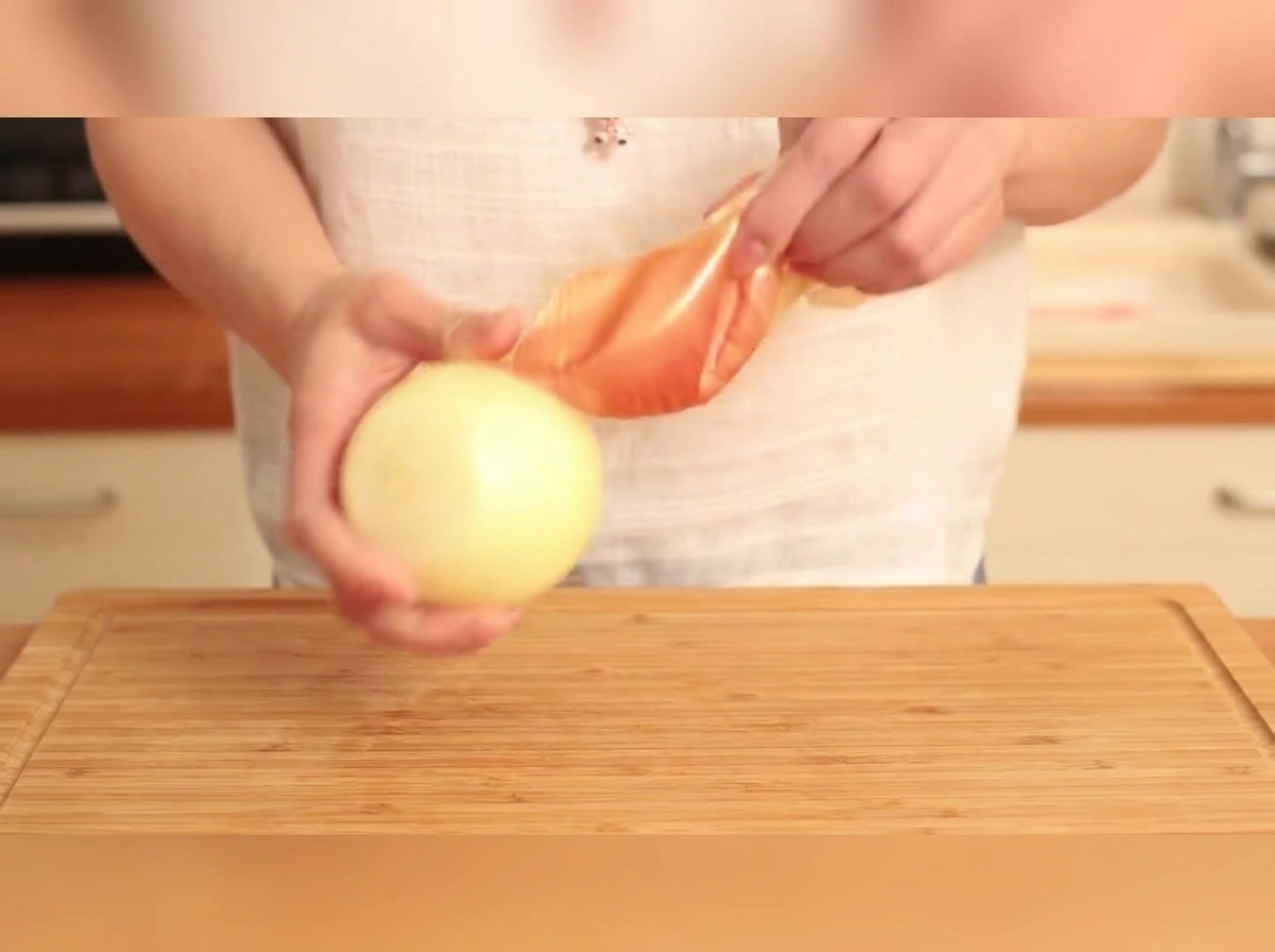 A peeled yellow onion being sliced into strips on a wooden cutting board.