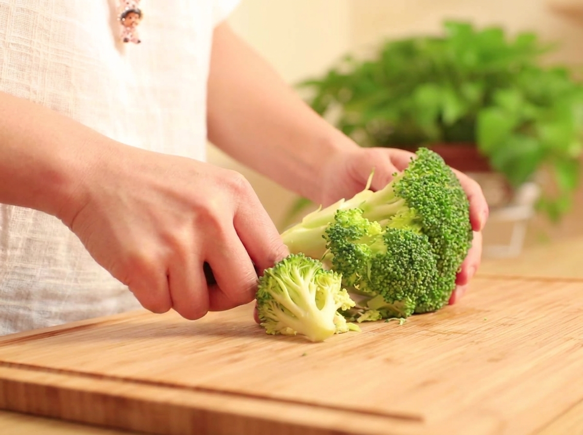 Fresh broccoli florets being separated on a wooden cutting board.