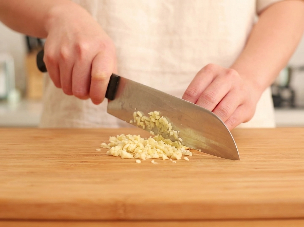 Fresh ginger and garlic being finely minced on a wooden surface.