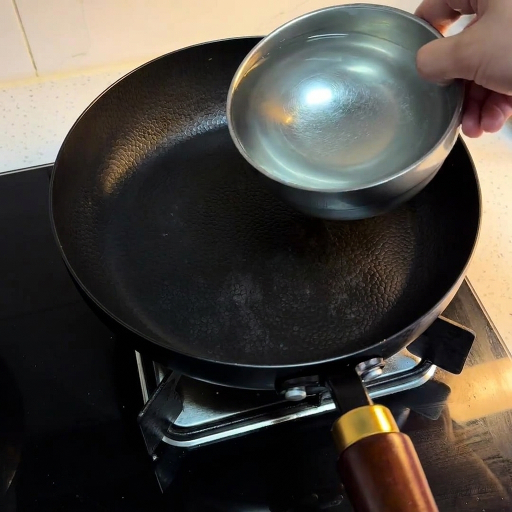 Three bowls of water being poured into a black pan resting on a stovetop burner.