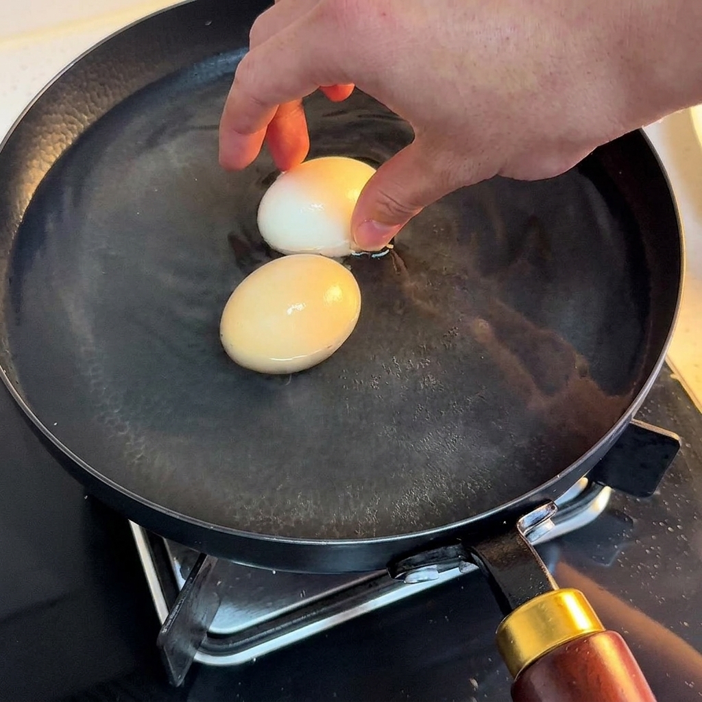 Two cooked eggs being transferred into a bowl of cold water.