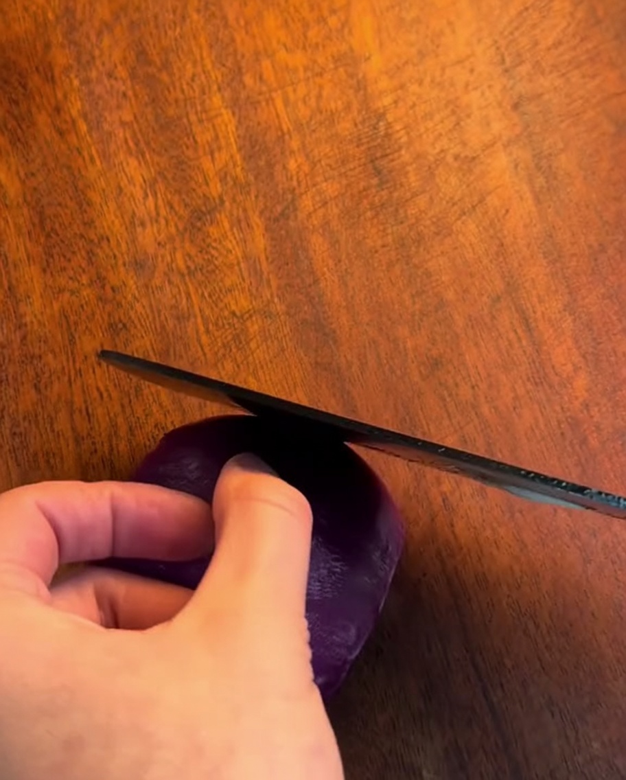 A sharp knife slicing an onion into thin, even strips on a wooden board.