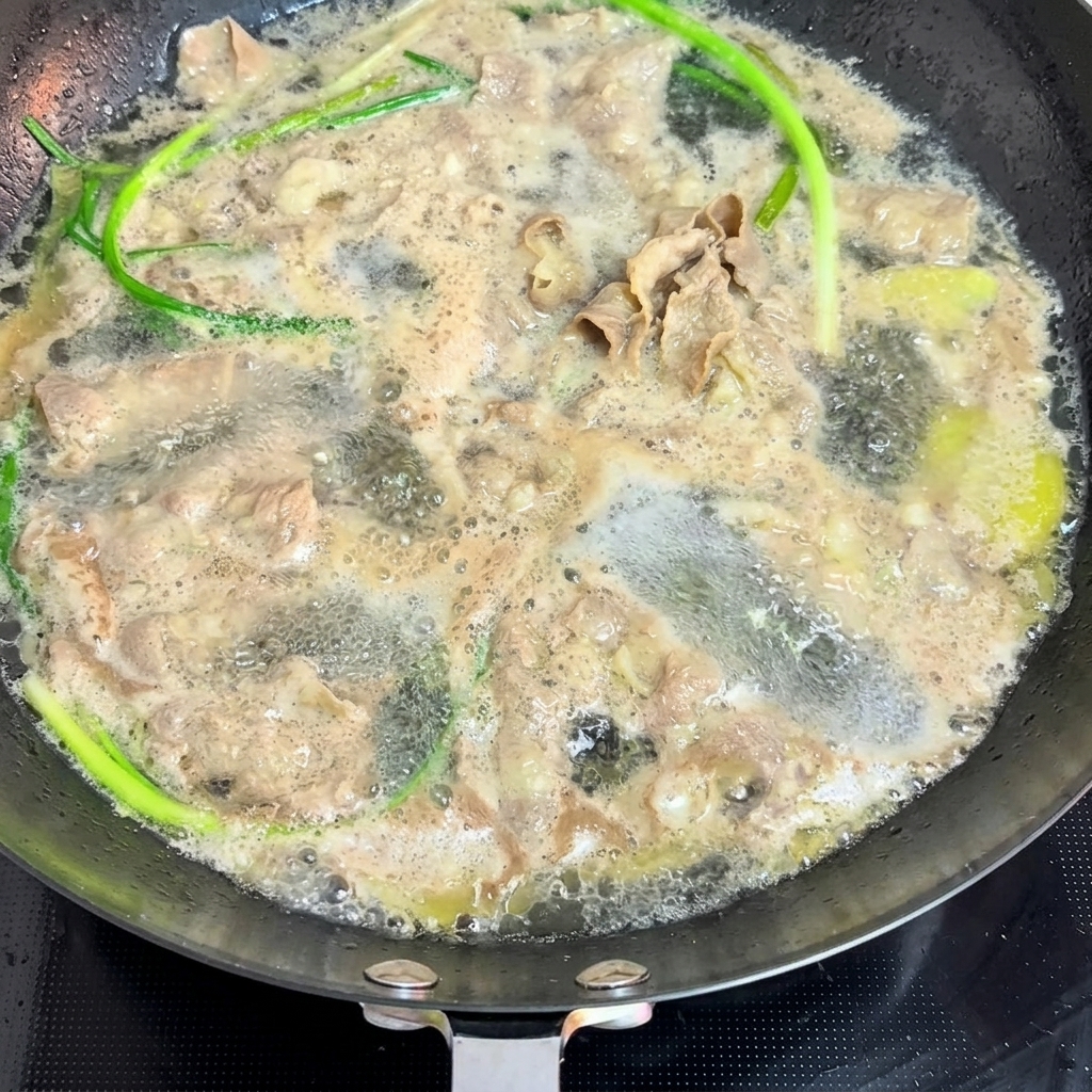 Thin slices of beef and fresh scallions being blanched in a pan of boiling water.