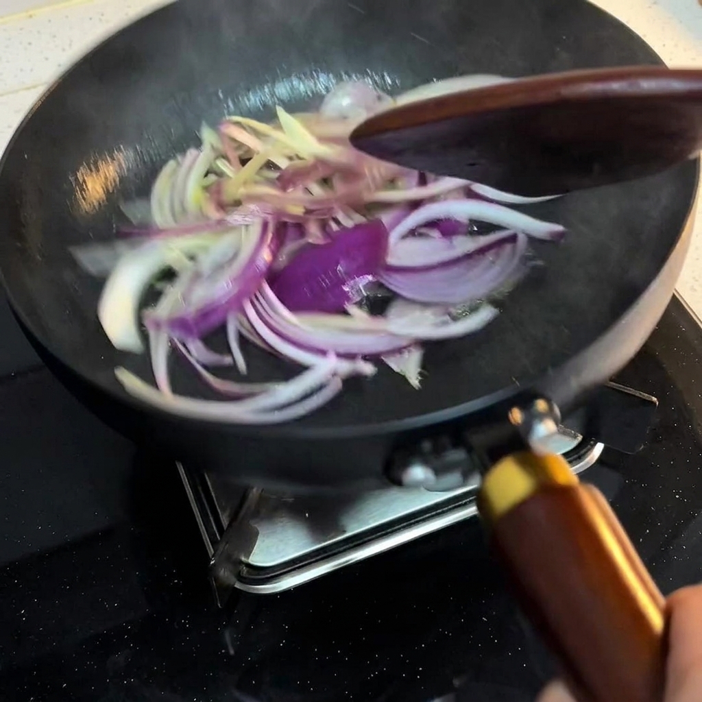 Onion slices being stirred in a pan with a wooden spatula over medium heat.